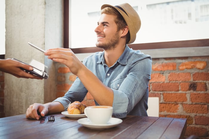 Handsome hipster paying with smartphone at coffee shop