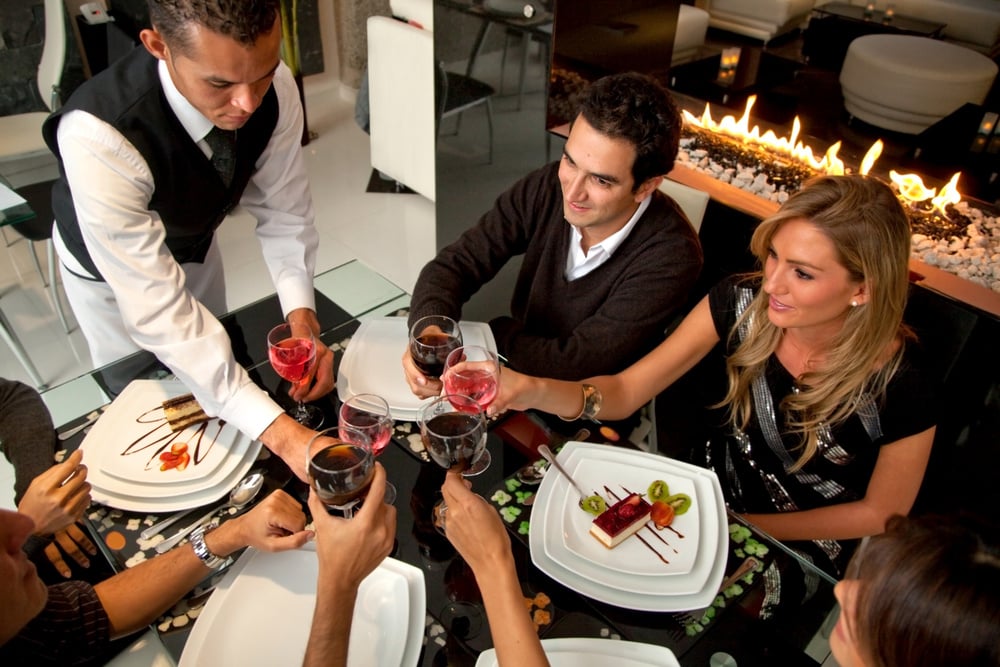 Group of people at a restaurat having dinner being served by a waiter